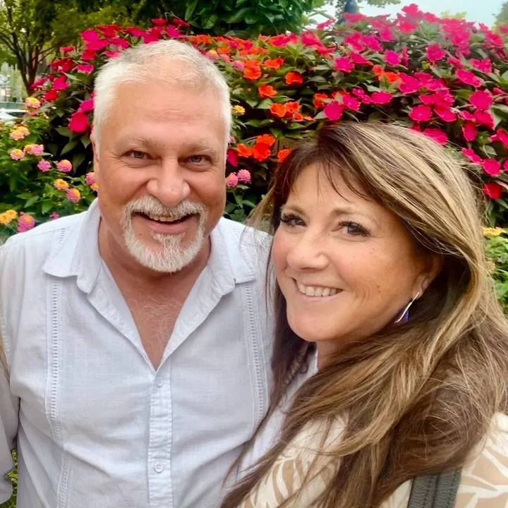 Martha "Marty" Giddings, broker and owner, RE/MAX Snowshoe, with Michael Hughes, smiling in front of a bed of flowers