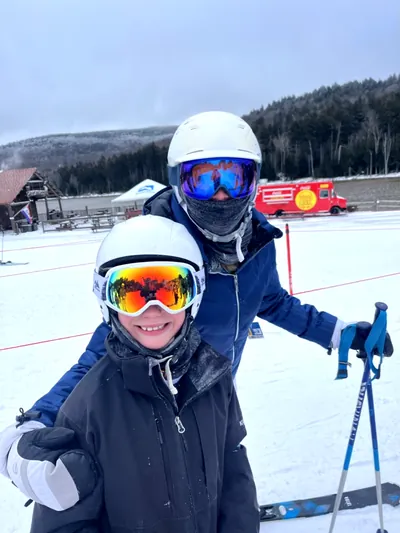 Two smiling young skiers in helmets and goggles at the base area