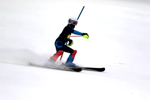 A young racer carving around a slalom gate with snow spraying off the skis