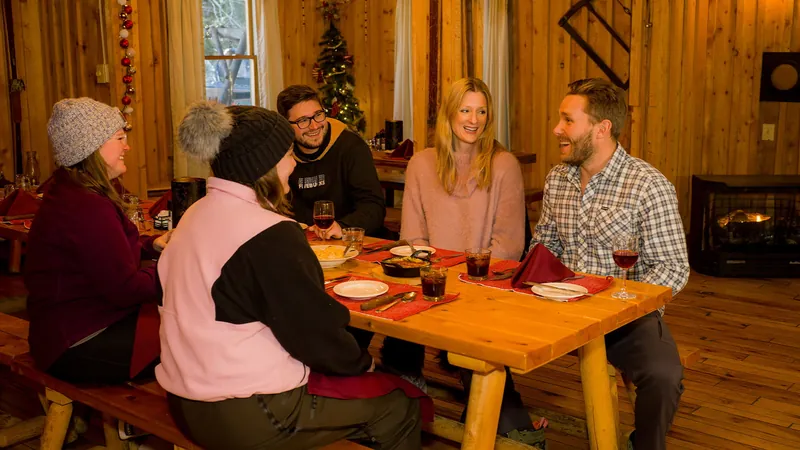 Guests sharing a meal at a wooden table inside the Sunrise Backcountry Hut