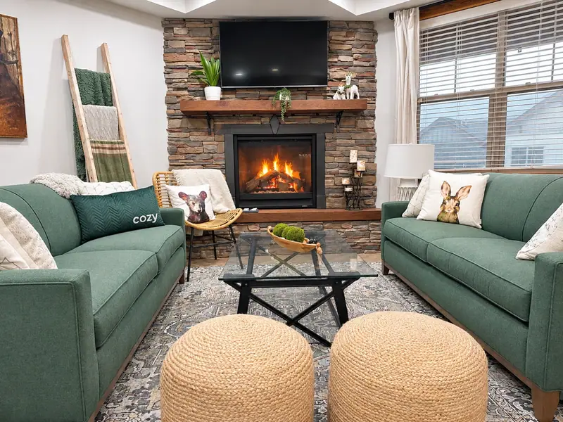 Living room at Black Bear 33 with two green sofas, a stone gas fireplace, and woven ottomans