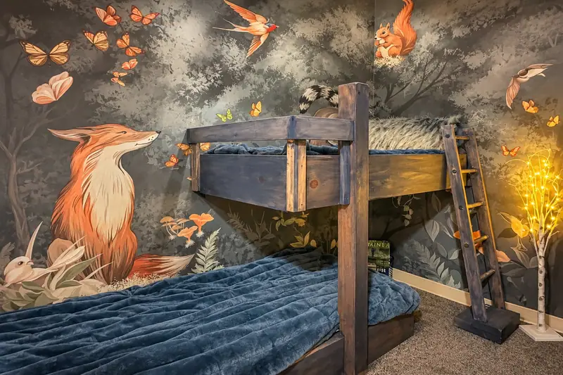 The enchanted forest room at Black Bear 33, a small bunk under a fox and woodland mural