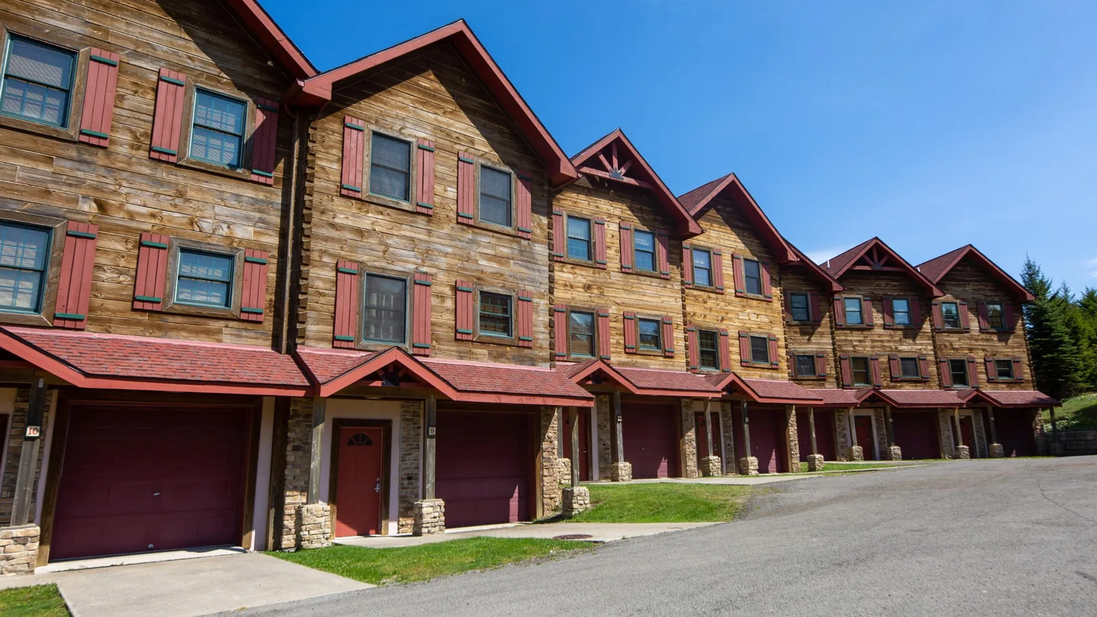 Loggers Run log townhomes with red trim and garage doors on a sunny summer day