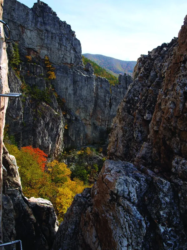 A narrow notch between two tall rock fins with autumn trees below, on the Via Ferrata at NROCKS