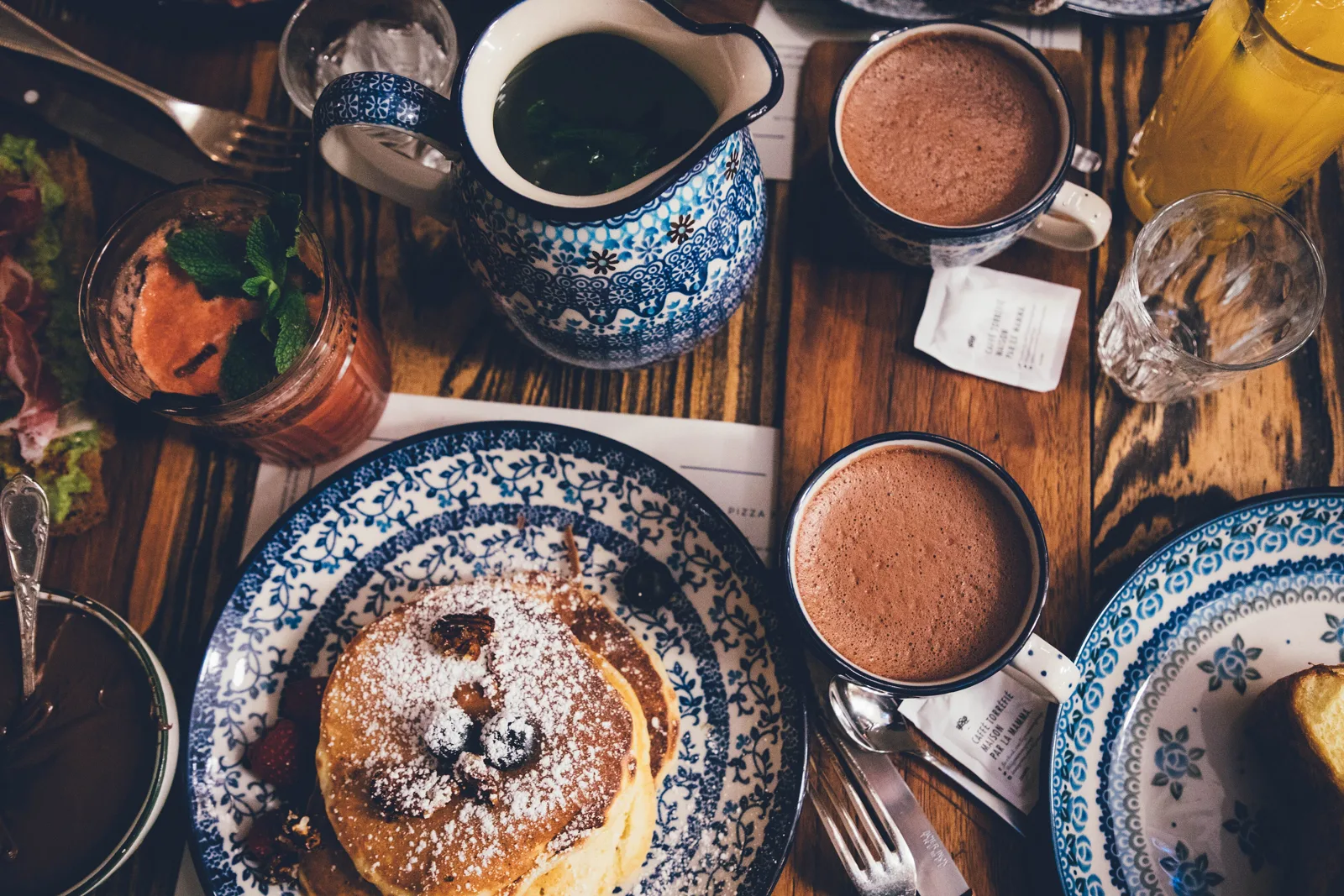 A breakfast table set with pancakes, hot cocoa, coffee, and fruit