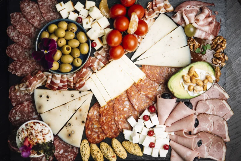 A charcuterie board with sliced meats, cheeses, olives, tomatoes, and crackers
