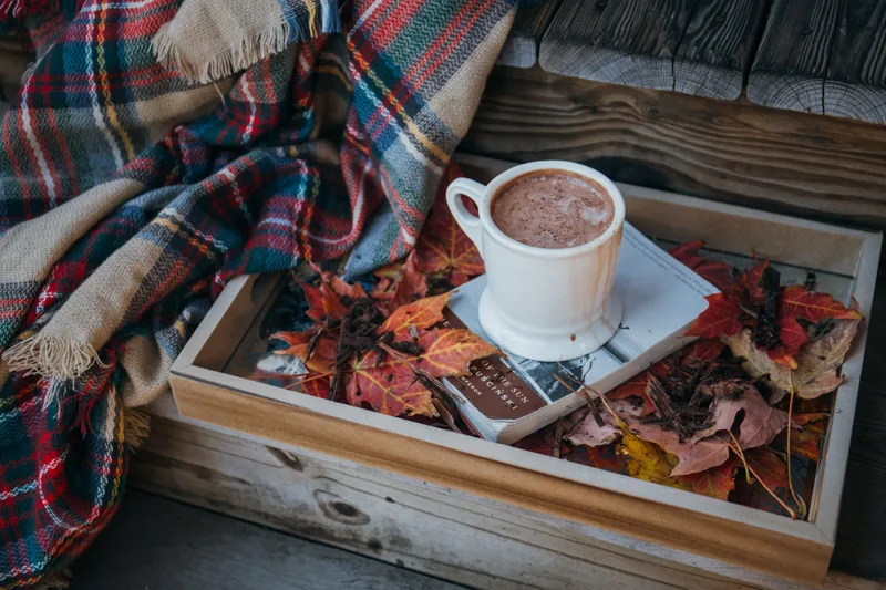 A mug of hot cocoa on a wooden tray with a plaid blanket
