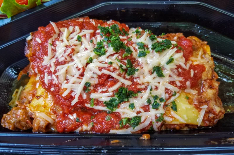 A tray of baked lasagna topped with tomato sauce, cheese, and parsley