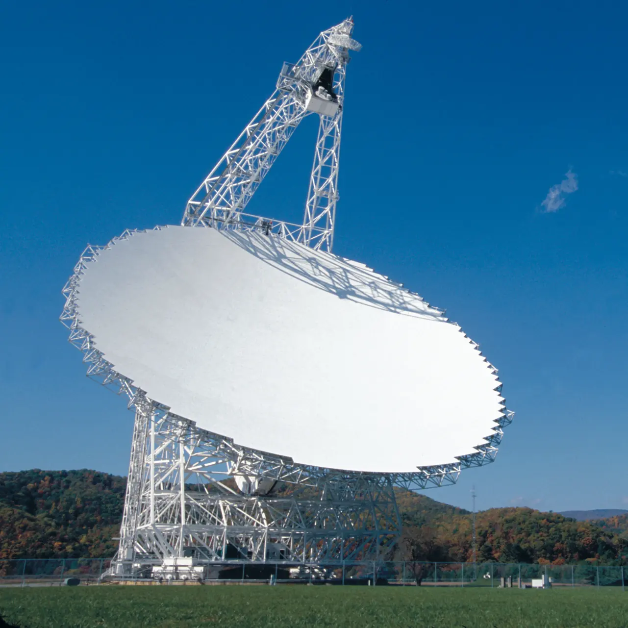 The Green Bank Telescope against a blue sky, with fall color on the ridge behind it