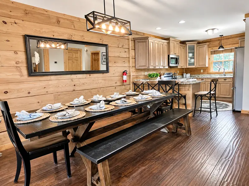 Dining table at Loggers Run 16 with bench seating under an iron chandelier, set for a group, with the kitchen beyond