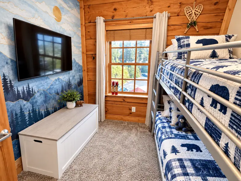 Bunk room at Loggers Run 4 with blue plaid bunks, a wall TV and a forest mural