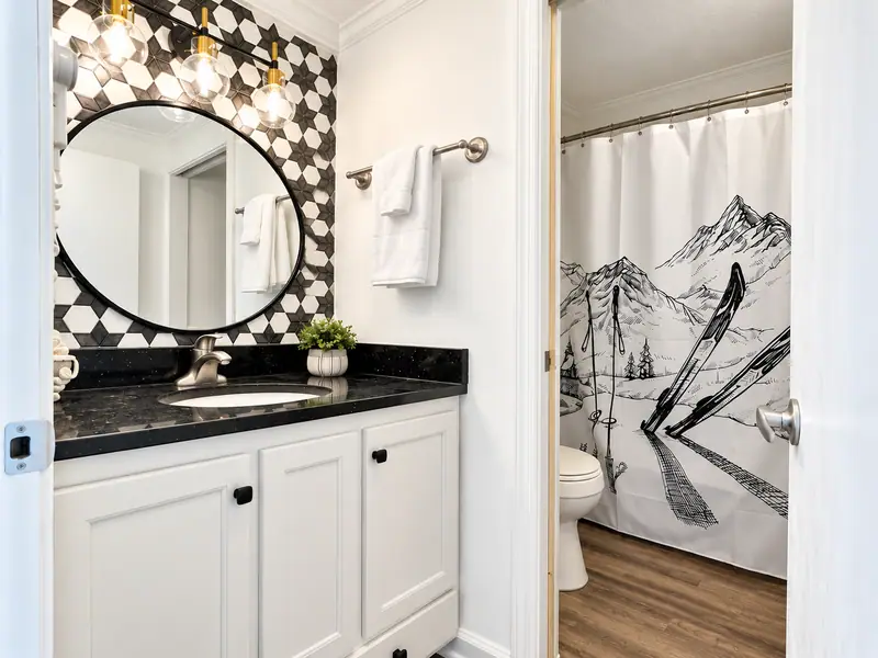 Bathroom vanity at Mountain Lodge 140 with a round mirror and patterned tile wall