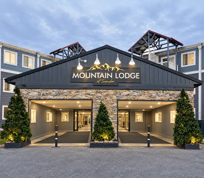 The Mountain Lodge entrance at dusk with a lit porte-cochere and evergreens