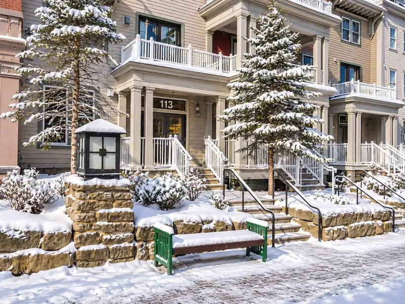 The Seneca porch entrance under fresh snow, with a green bench