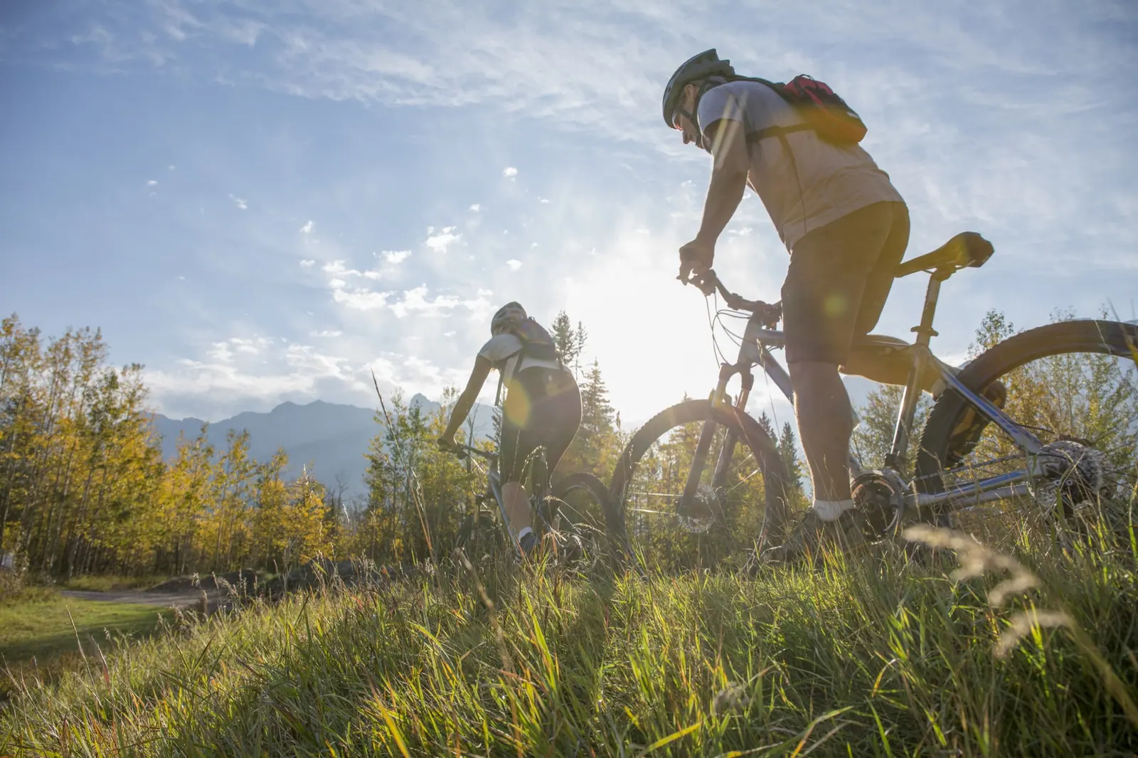 Two mountain bikers riding a grassy ridge trail in the sun